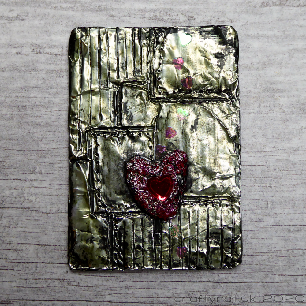 An art card covered with foil and "engraved" to look like riveted metal panels with a foil heart on it.